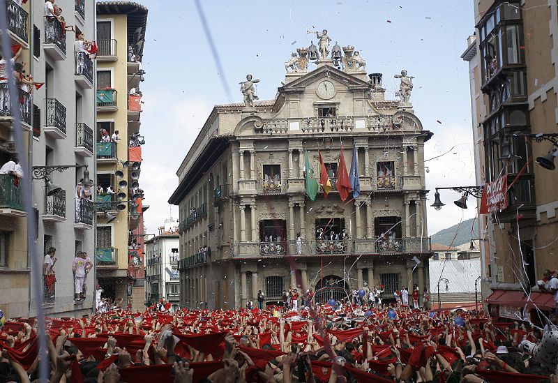 People hold up their red scarves to celebrate as streamers and confetti fall during the launch of the traditional rocket "Chupinazo" kicking off the annual San Fermin festival in Pamplona