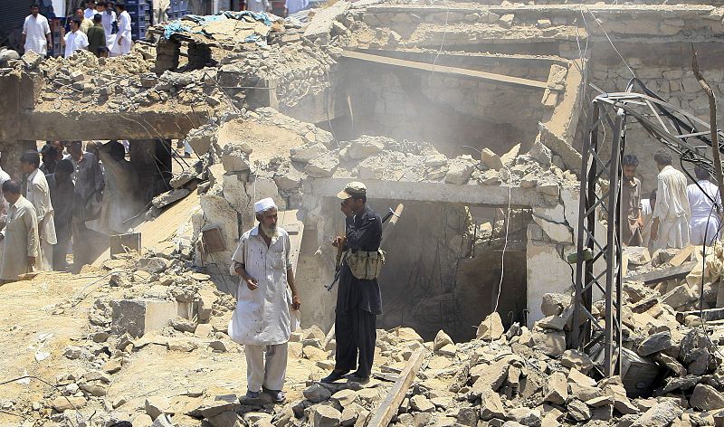 A policeman covers his mouth to protect against the dust as rescue workers and residents look at the aftermath of a suicide bomb blast in Pakistan's Mohmand ethnic Pashtun tribal region