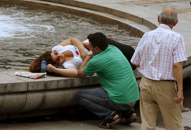 Una pareja conversa relajada en una fuente de la madrileña Plaza de España ante las altas temperaturas que azotan a la capital.