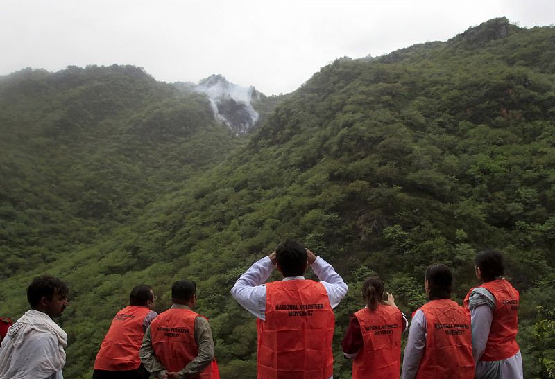 Volunteers on a rescue operation observe as smoke rises from the wreckage of a passenger plane which has crashed in the Margalla Hills on the outskirts of Islamabad