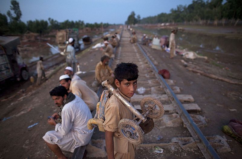 An Afghan immigrant holds his belongings while standing among thousands of flood victims taking refuge along a railroad track in Pabbi