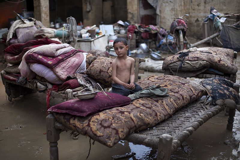 Inamullah, 4, sits amidst furniture left to dry in a flooded courtyard after returning to his house in Nowshera