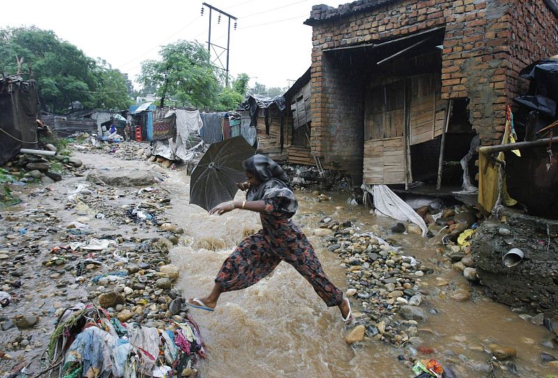 Una mujer salta por encima de las aguas de las inundaciones en frente de su casa dañada tras las fuertes lluvias en Jammu (India)