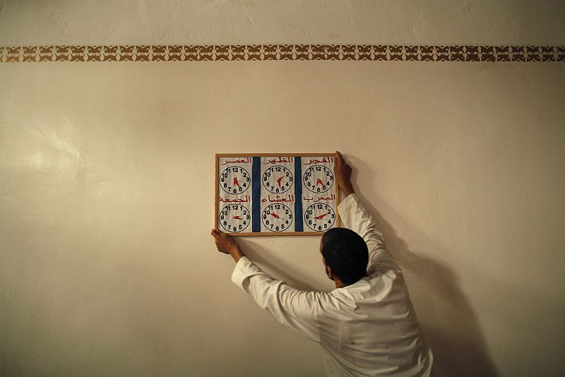 A Muslim man places a table which marks the times to pray on a wall during the first day of Ramadan at a mosque in Estepona