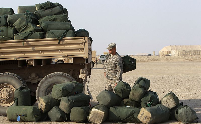 A U.S. soldier from the 1st Battalion, 116th Infantry Regiment, waits to load his bag onto a military vehicle carrying other bags as he prepares to leave Iraq for Kuwait