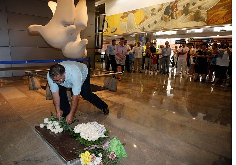 Un miembro de la Asociación de Afectados del Vuelo JK5022 deposita un ramo de rosas sobre la placa que recuerda a las víctimas en el aeropuerto de Barajas.