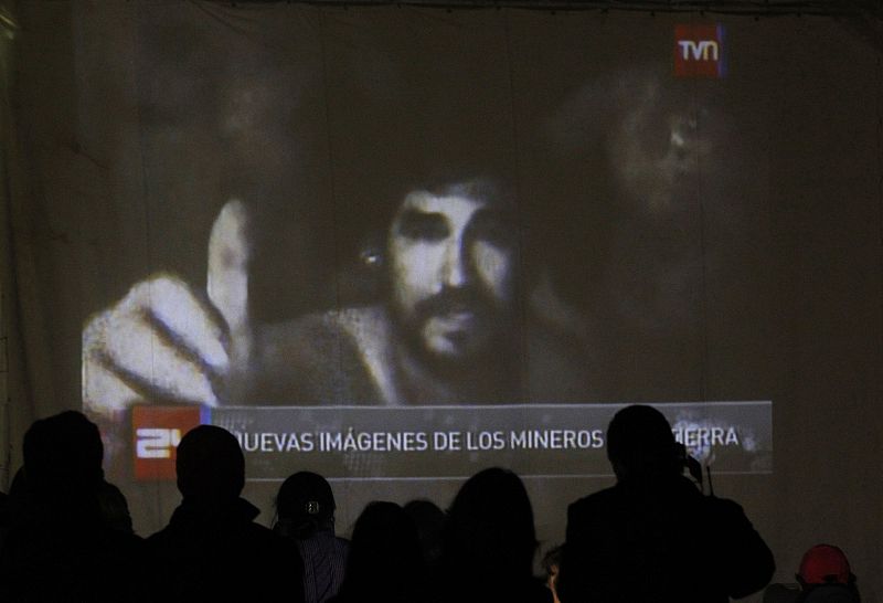 Relatives of the miners trapped underground in a copper and gold mine, gather around a screen that shows the miners inside the mine at Copiapo