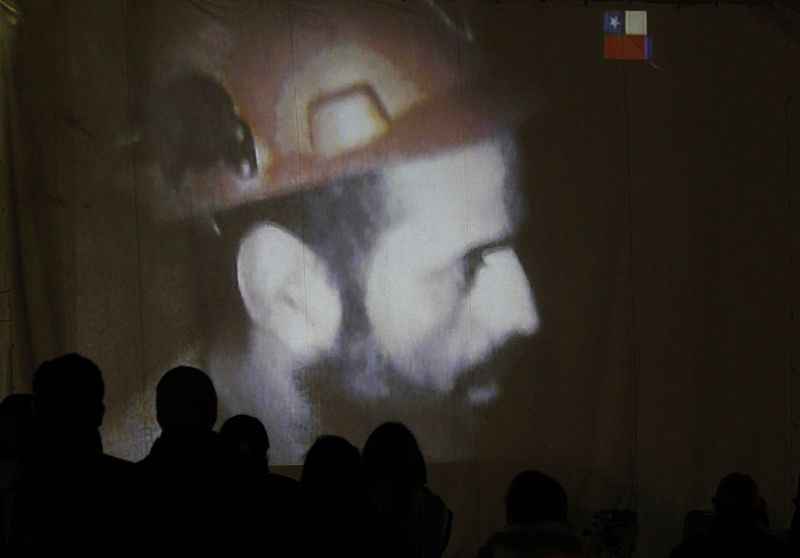 Relatives of the miners trapped underground in a copper and gold mine gather around a screen that shows miners inside the mine at Copiapo