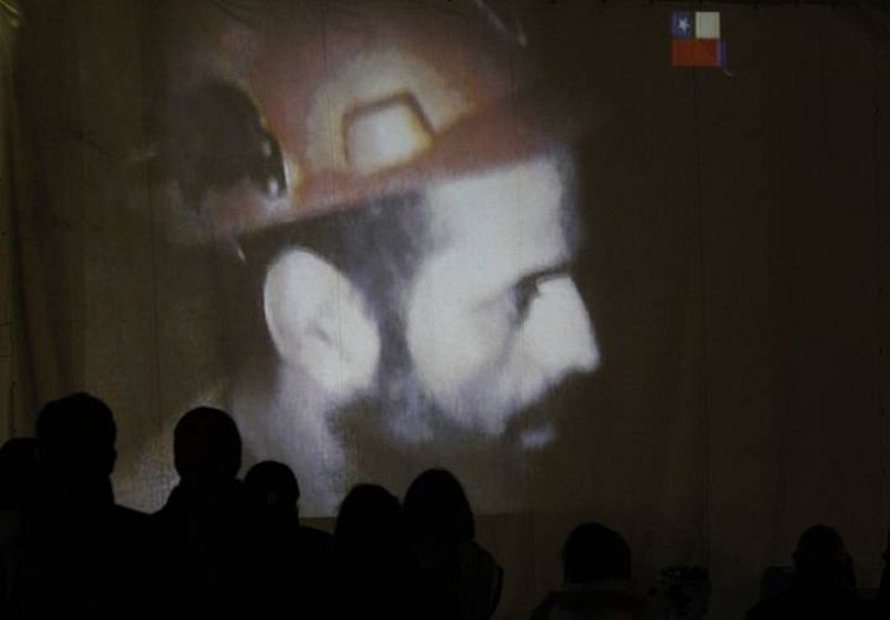 Relatives of the miners trapped underground in a copper and gold mine gather around a screen that shows miners inside the mine at Copiapo