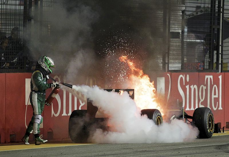 El piloto de Lotus Heikki Kovalainen intenta apagar el fuego de su coche, tras una avería.