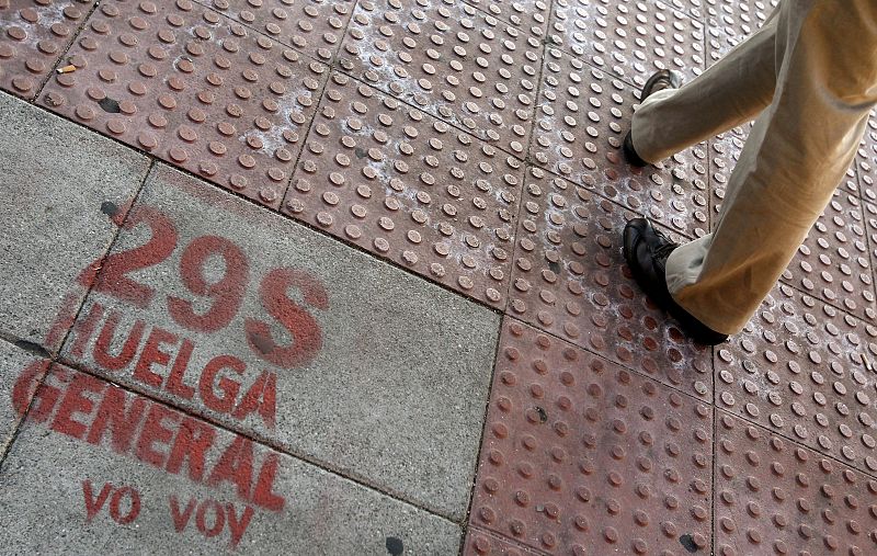 Un hombre camina junto a un grafitti pintado en el suelo que dice "29S huelga general. Yo voy", en la Plaza Castilla en Madrid.