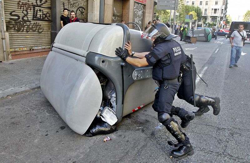 Varios mossos d'esquadra apartan un contenedor usado para formar una barricada durante los incidentes de Barcelona por la huelga general.