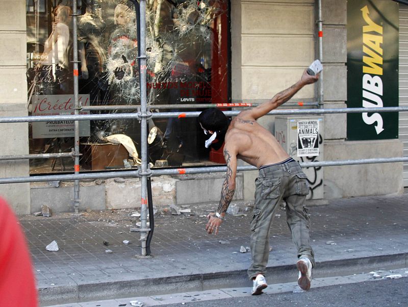 A protester throws a rock at the window of a clothing store during a general strike in central Barcelona