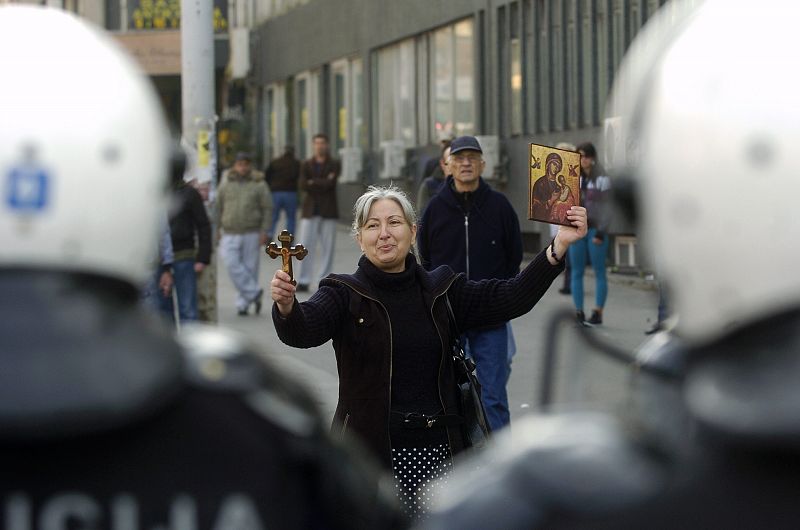 A woman holds a cross and a religious icon as she stands in front of riot police during riots in Belgrade