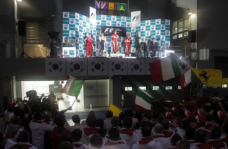 Members of the Ferrari Formula One team wave Italian and Ferrari flags as their drivers Fernando Alonso of Spain and Felipe Massa of Brazil stand on the podium after winning the South Korean F1 Grand Prix at the Korea International Circuit in Yeongam