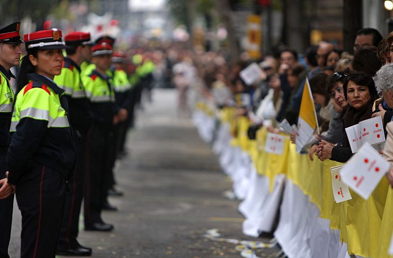 Varios mossos d'Esquadra mantienen un cordón de seguridad junto a los fieles que esperan impacientes tras las vayas a que pase el Papa.