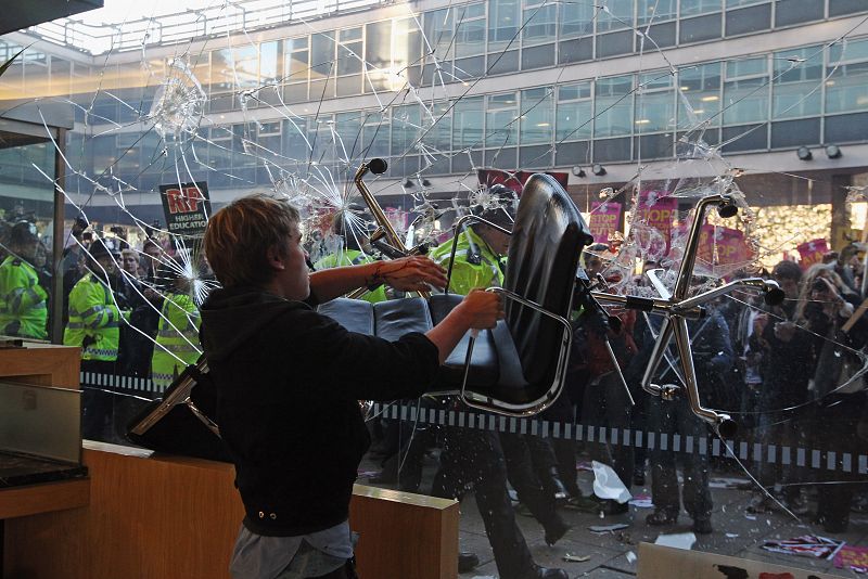 Uno de los estudiantes que han ocupado la sede del Partido Conservador británico rompe la ventana del edificio con una silla.