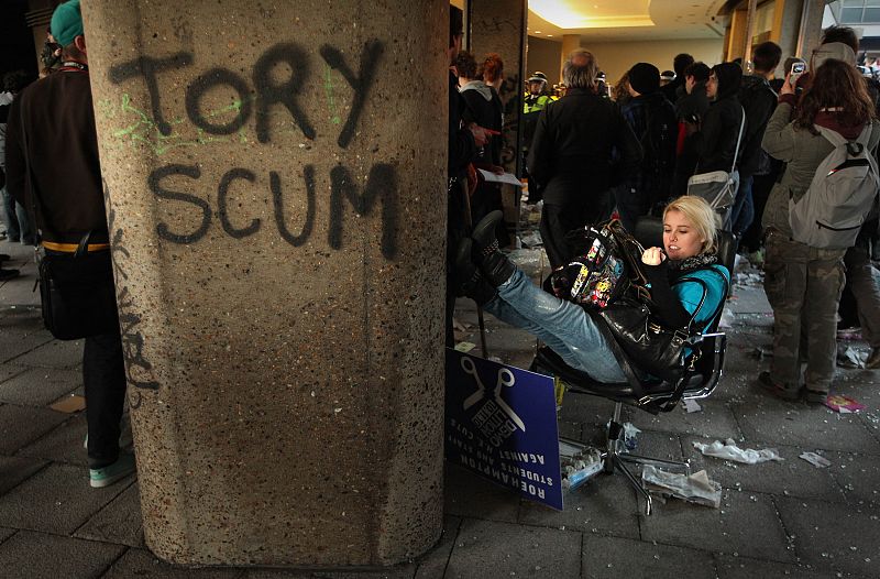 Una estudiante se sienta en una de las sillas de oficina de la sede 'tory' frente a una pintada en un muro en la que se lee "Escoria tory".