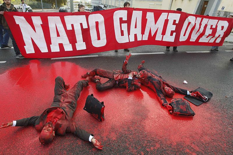 People lie in red paint on a road during protests against the NATO summit in Lisbon