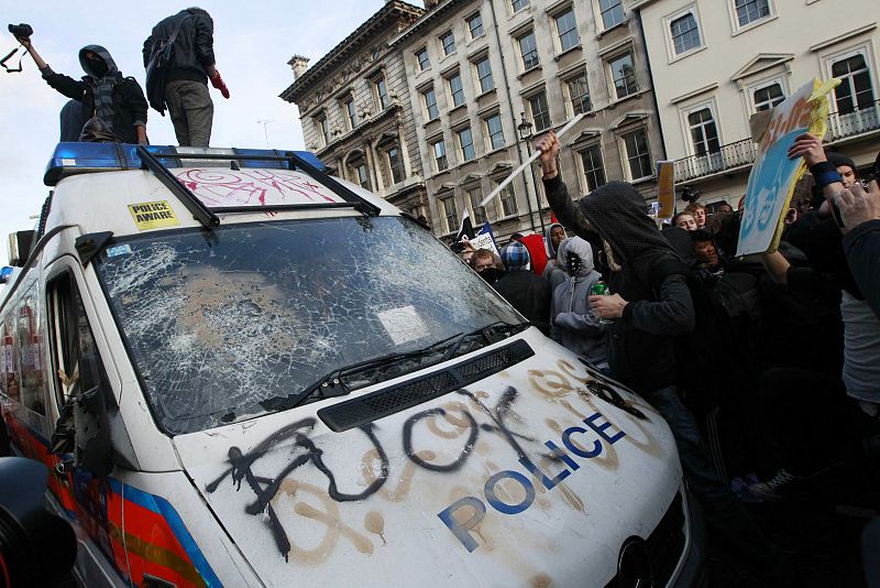 Los manifestantes atacan un coche policial, al que han roto los cristales, pintado y zarandeado.