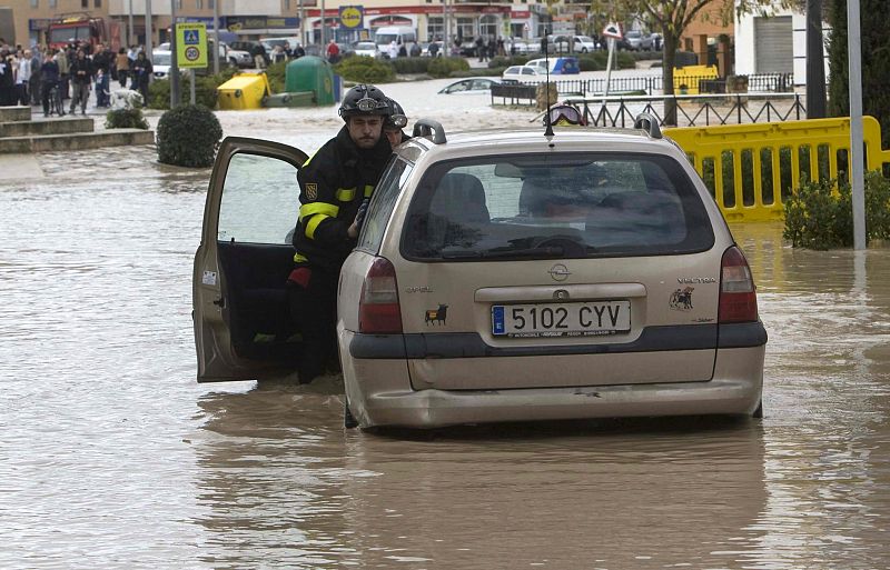 Bomberos intentan sacar un automóvil de una calle anegada del casco urbano de Écija