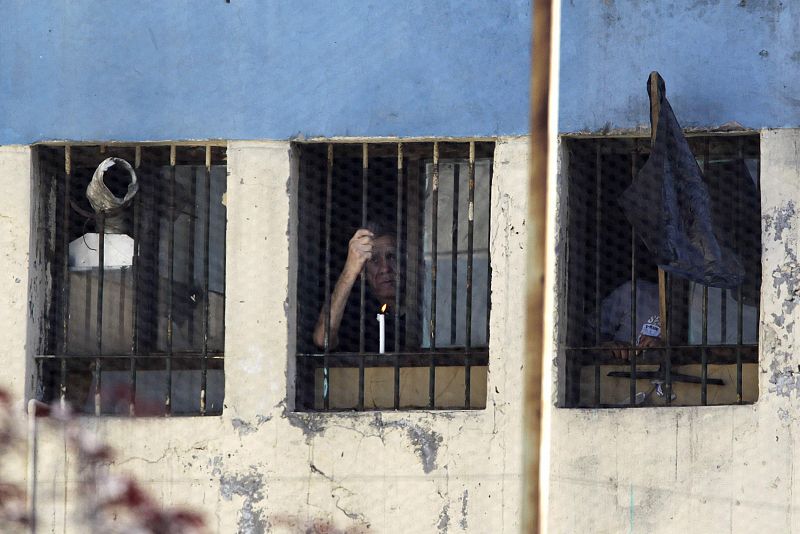 Uno de los reclusos, con una vela en la mano, mira por la ventana de su celda