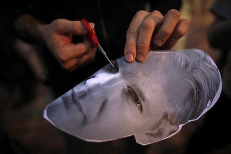 A protester cuts holes into the eyes of a mask of WikiLeaks founder Julian Assange as he takes part in a demonstration to call for the release of Assange, in Malaga