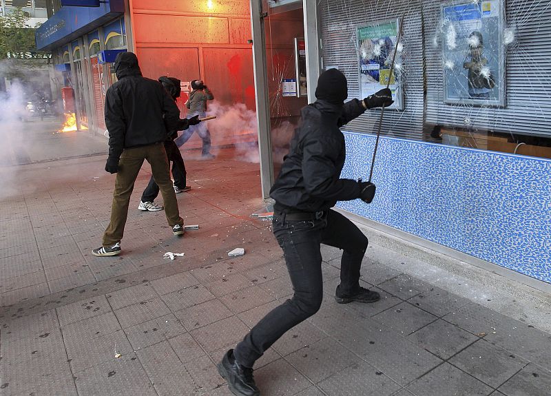 Un manifestante rompe un escaparate a las puertas ministerio de Finanzas griego delante de varios policías antidisturbios.