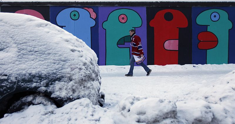 A man walks past a snow-covered car parked at the East Side Gallery in Berlin