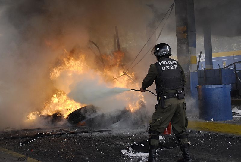 Un policía intenta apagar el fuego de uno de los puestos de la autopista que une La Paz y El Alto