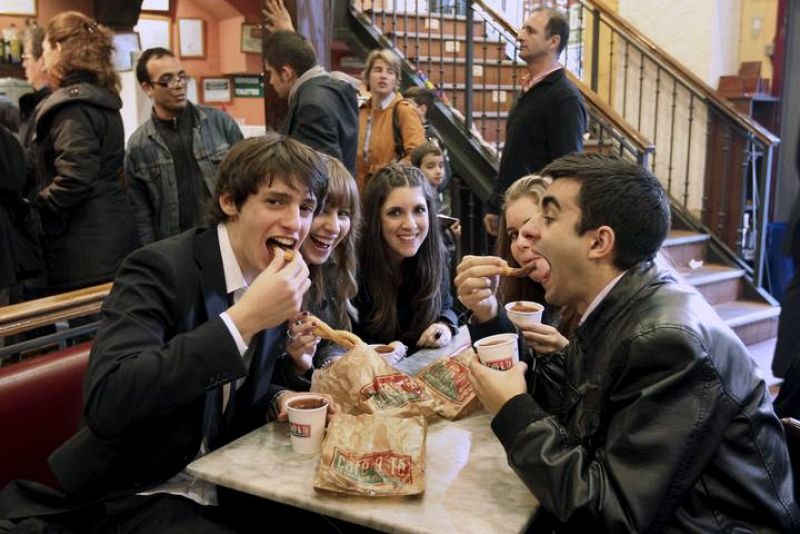 Un grupo de jóvenes toman el tradicional chocolate con churros a primeras horas de la mañana en un local madrileño, tras la celebración de la Nochevieja y el Año Nuevo la pasada madrugada