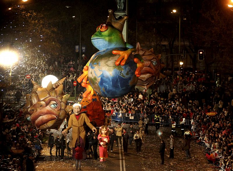 Cientos de personas observan el paso de dos marionetas gigantes que representan a un abuelo y su nieta durante la cabalgata de Reyes de Madrid