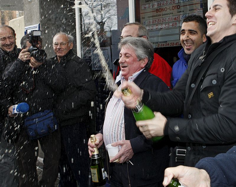 José Luis Nieto (c), regente de la administración de loterías número 247 de Madrid, ubicada en el popular barrio de Ascao (Ciudad Lineal), donde se ha vendido íntegramente el número 70.013, primer premio del sorteo de la lotería de "El Niño"