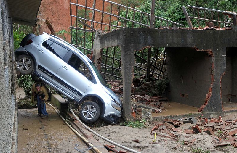 Un fotógrafo local se cuela por debajo de un coche para captar los destrozos de las lluvias.