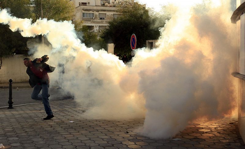 Un manifestante tira uno de los botes de gases lacrimógenos de la policía durante los disturbios de Túnez.