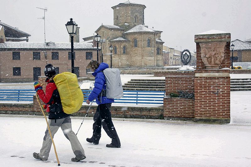 Dos peregrinos pasan por delante de San Martín en Frómista (Palencia), localidad cubierta por la nieve