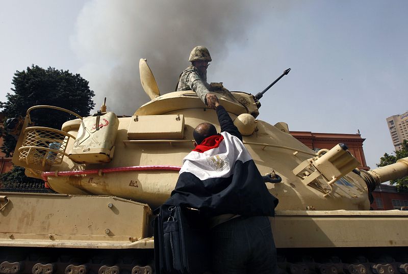 A protester draped in an Egyptian flag climbs atop an army tank to shake hands with a soldier in Cairo