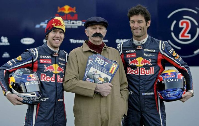 Los pilotos del equipo Red Bull de Fórmula Uno, el campeón del Mundo el alemán Sebastian Vettel, y el australiano Mark Webber, posan con un figurante disfrazdo de mecánico de principios del siglo XX.