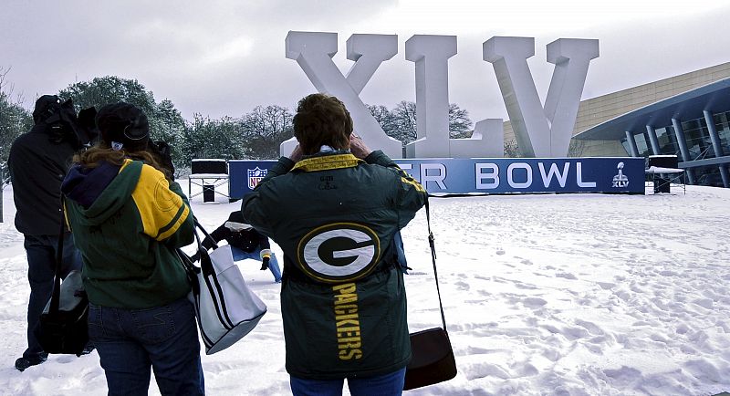 El frío y la nieve tiñen de blanco el escenario de la final de la Super Bowl. Dos aficionados toman fotografías del logo de la Super Bowl en el estadio Cowboy de Dallas