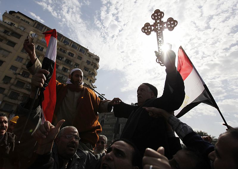 A Muslim holding the Koran and a Coptic Christian holding a cross are carried through opposition supporters in Tahrir Square in Cairo