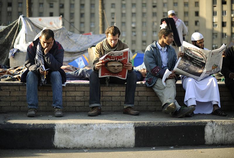 Anti-government protesters read the newspapers as they wake up inside Tahrir Square in Cairo