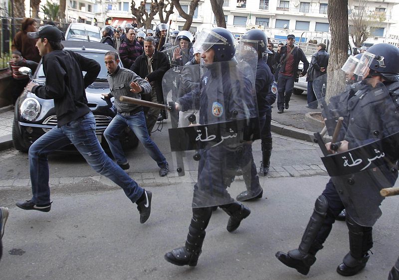 Riot police run behind a protester during a demonstration in Algiers