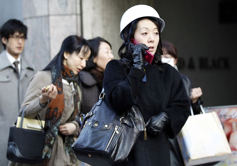 Woman wears hard hat and talks on phone after evacuating building in Tokyo's financial district, after earthquake off the coast of northern Japan