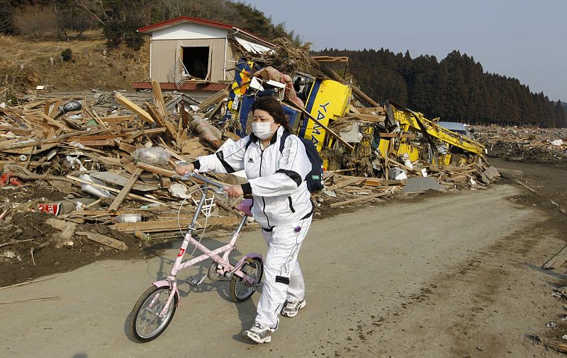A woman pushes a bicycle as she walks through the rubble in Rikuzentakata, northern Japan after the magnitude 8.9 earthquake and tsunami struck the area