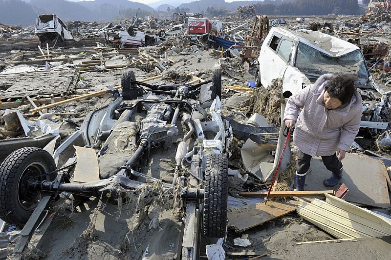 A woman searching for her missing husband looks under an overturned truck after an earthquake and tsunami struck Minamisanriku, Miyagi Prefecture