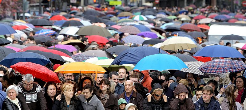 Numerosas personas se protegen de la lluvia que cae de forma intermitente sobre Valencia, antes del disparo de la mascletá.