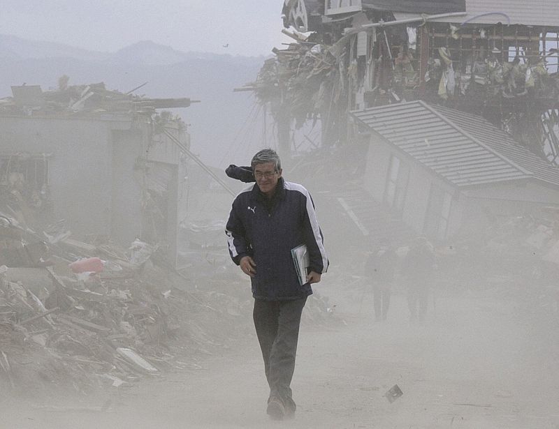 A man walks through rubble amidst dust blown up by wind in Rikusentakata City