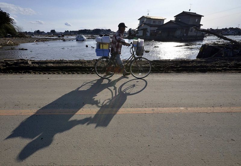 A man pulls a bicycle along a road, with a view of the area struck by last week's earthquake and tsunami, outside Sendai in Miyagi Prefecture, northern Japan