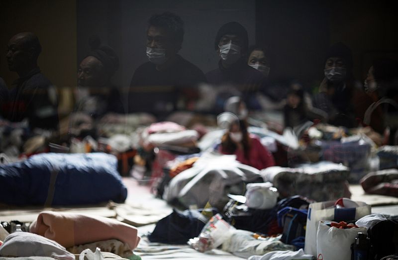 Earthquake and tsunami survivors are reflected in the window of a collective shelter as they wait for food to be distributed in Kesennuma