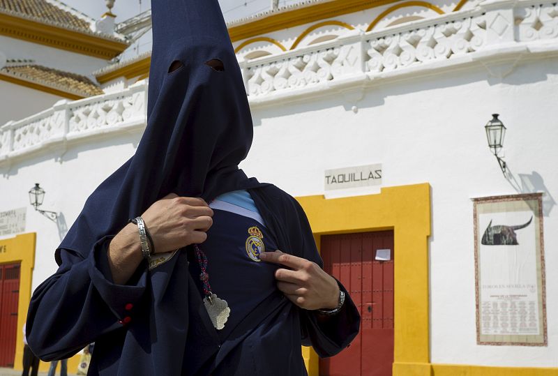 Un nazareno de la Hermandad del Baratillo muestra bajo su túnica una camiseta con el escudo del Real Madrid junto a la plaza de toros de la Real Maestranza de Sevilla